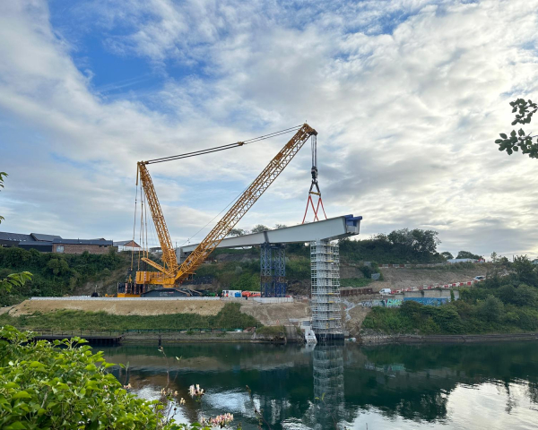 Crane lifting a section of the bridge into place on a sunny day.